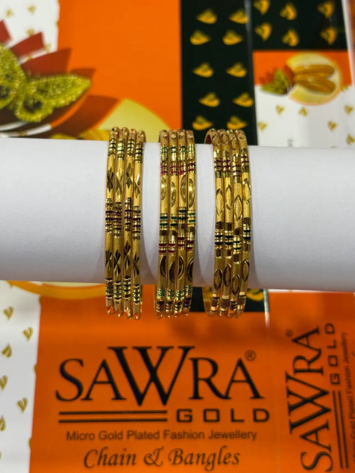 Three gold-plated bangles with intricate geometric and floral engravings, displayed on a white cylindrical stand. The background features branded packaging for SAWRA GOLD.