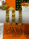 Three gold-plated bangles with intricate patterns displayed on a white cylindrical stand, with an orange SAWRA GOLD brand box in the background.