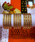 A set of gold-plated bangles with intricate floral and leaf patterns, displayed on a white cylindrical stand. The background features branded packaging for SAWRA GOLD.