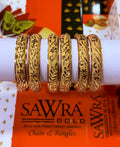 Six ornate gold bangles with intricate floral and geometric patterns, displayed on a white cylindrical stand. The brand name 'SAWRA GOLD' is visible on the orange packaging below.
