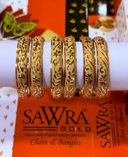 Six ornate gold bangles with intricate floral and geometric patterns, displayed on a white cylindrical stand. The brand name 'SAWRA GOLD' is visible on the orange packaging below.
