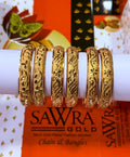 Five ornate gold bangles with intricate floral and leaf engravings displayed on a white cylindrical stand. The background features branding for SAWRA GOLD.