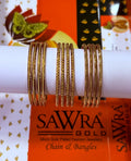 Three gold-plated bangles displayed on a white cylindrical stand, with a branded orange and white SAWRA GOLD box in the background.