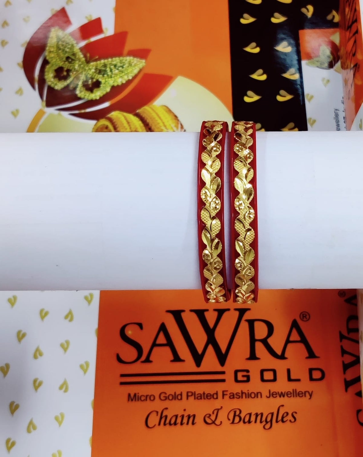 Gold bangles on a white surface with Sawra Gold packaging in the background.