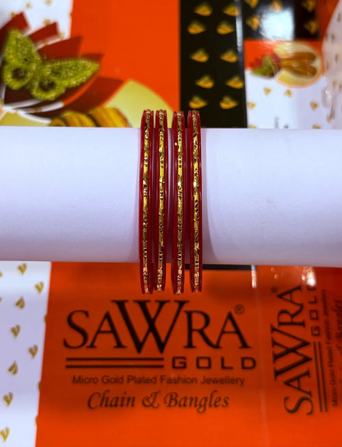 Five red bangles with gold foil patterns wrapped around a white cylindrical display stand, with SAWRA GOLD branding visible in the background packaging.