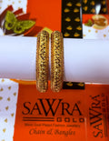 Two gold-plated bangles with a textured, diamond-patterned surface, displayed on a white cylindrical stand in front of an orange SAWRA GOLD brand box.
