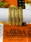 Four gold chain and bangle bracelets displayed on a white cylindrical stand, with an orange SAWRA GOLD brand card visible underneath.